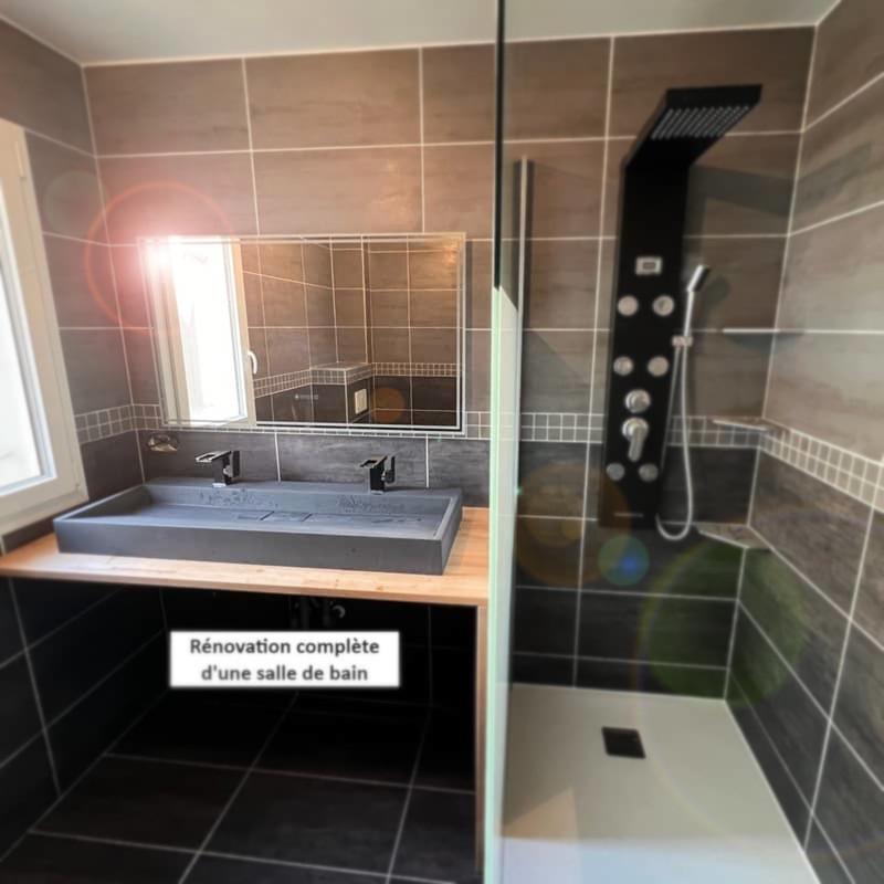 Salle_de_bain Salle de bain rénovée avec une douche italienne moderne, colonne de douche design noire, et un lavabo double vasque sur un plan en bois.