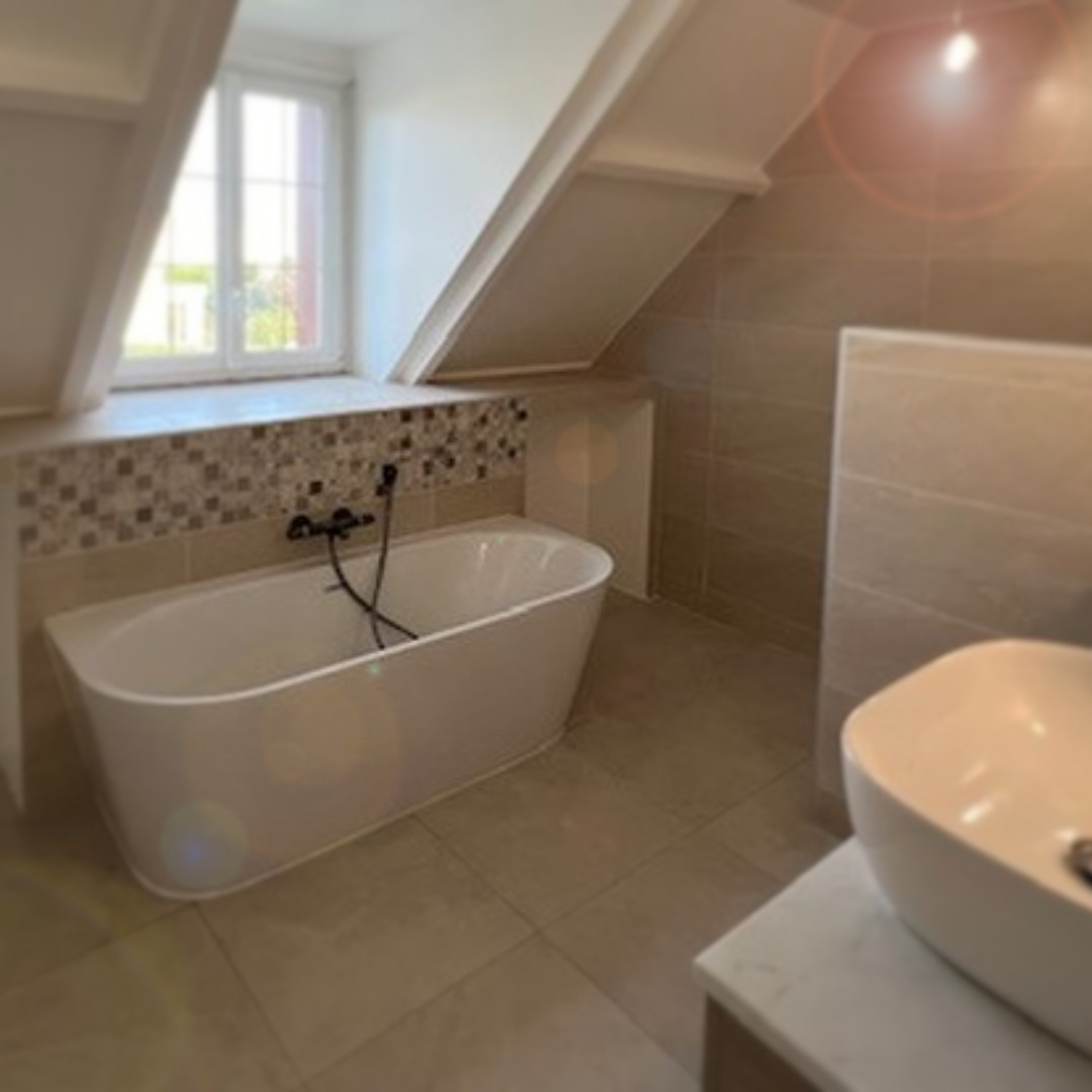 Salle_de_bain_01 Salle de bain rénovée sous combles avec baignoire îlot moderne, revêtement en carrelage beige et mosaïque murale.
