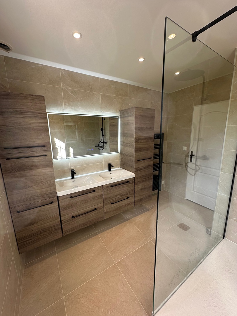 Salle de bain la chapelle sous gerberoy_2 Salle de bain rénovée à Osny (Val-d’Oise), au style contemporain et épuré. Revêtement mural effet béton, meuble en bois clair avec vasque moderne et miroir rétroéclairé. Baignoire îlot design, niche murale lumineuse et touche végétale suspendue pour une ambiance zen.