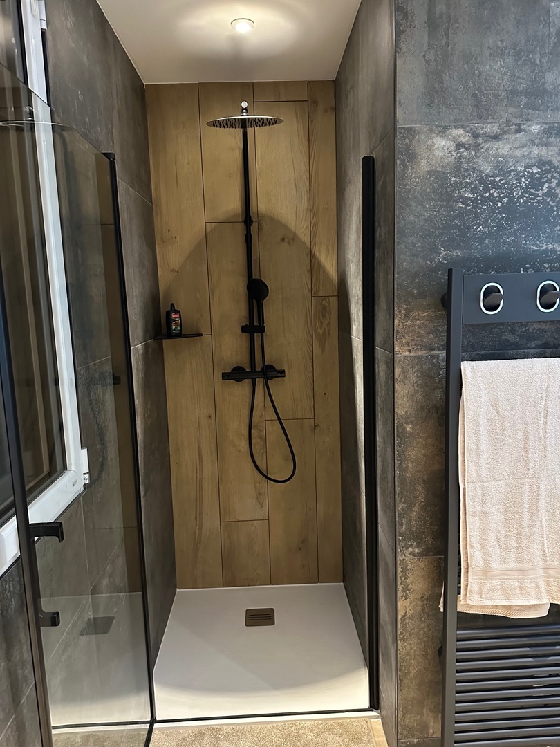 Salle de bain osny Salle de bain rénovée sous combles avec baignoire îlot moderne, revêtement en carrelage beige et mosaïque murale.