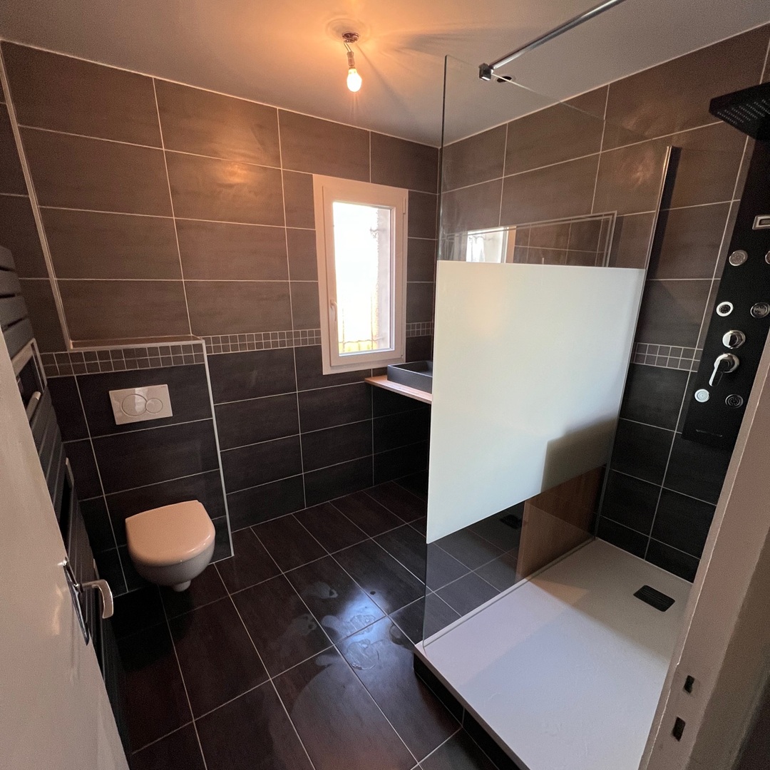 sdb boissy l aillerie Salle de bain rénovée à Osny (Val-d’Oise), au style contemporain et épuré. Revêtement mural effet béton, meuble en bois clair avec vasque moderne et miroir rétroéclairé. Baignoire îlot design, niche murale lumineuse et touche végétale suspendue pour une ambiance zen.