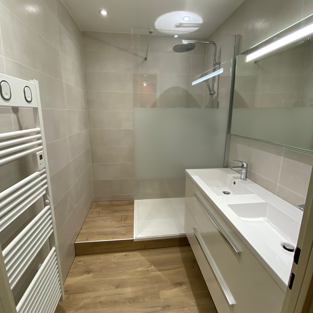 sdb clos de fleurance Salle de bain rénovée sous combles avec baignoire îlot moderne, revêtement en carrelage beige et mosaïque murale.
