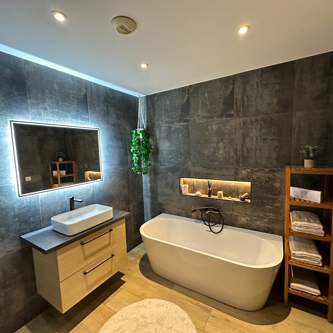 sdb osny Salle de bain rénovée à Osny (Val-d’Oise), au style contemporain et épuré. Revêtement mural effet béton, meuble en bois clair avec vasque moderne et miroir rétroéclairé. Baignoire îlot design, niche murale lumineuse et touche végétale suspendue pour une ambiance zen.
